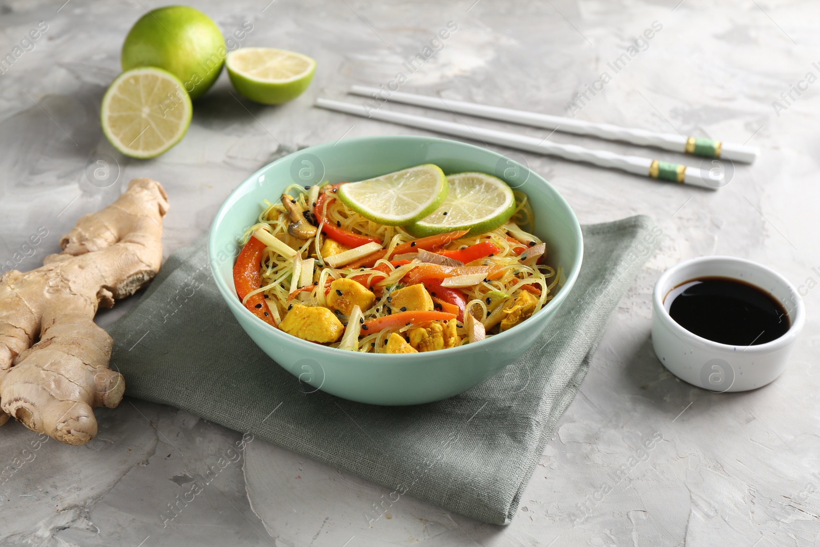 Photo of Stir-fry. Delicious cooked noodles with chicken and vegetables in bowl served on gray textured table