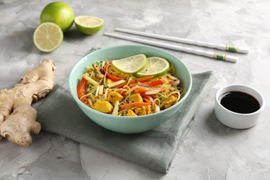 Photo of Stir-fry. Delicious cooked noodles with chicken and vegetables in bowl served on gray textured table