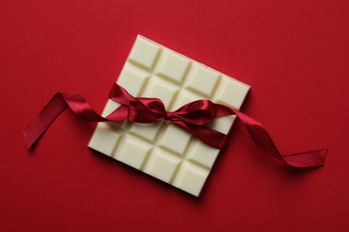 Tasty white chocolate bar with ribbon on red background, top view