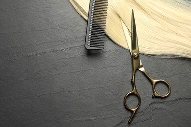 Photo of Professional hairdresser scissors and comb with blonde hair strand on dark grey table, flat lay. Space for text