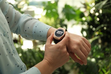 Woman checking home security system via smartwatch app outdoors, closeup. Image of room through CCTV camera on display