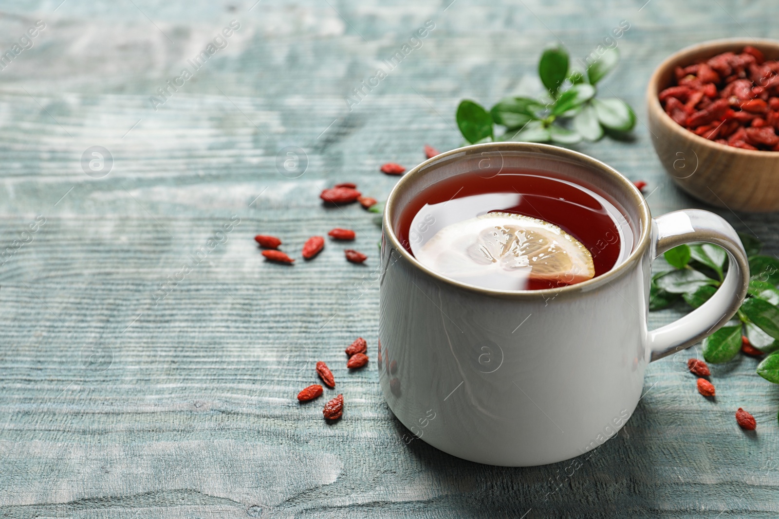 Photo of Healthy goji tea with lemon in cup on blue wooden table. Space for text