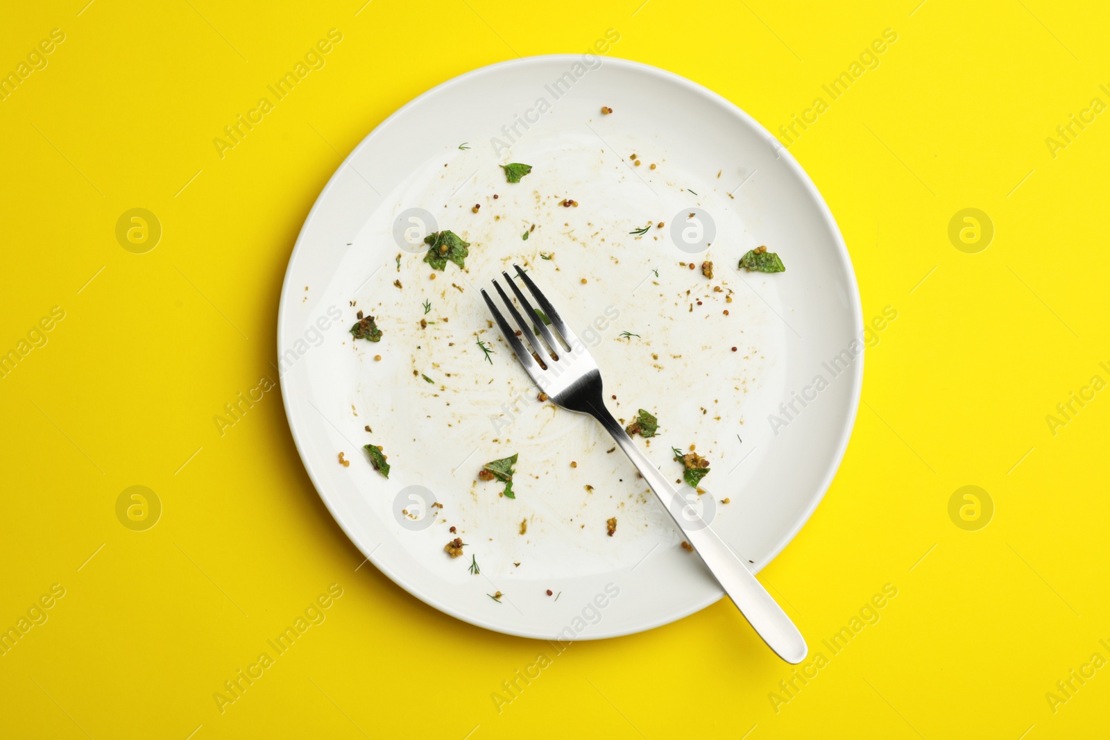 Photo of Dirty plate with food leftovers and fork on yellow background, top view