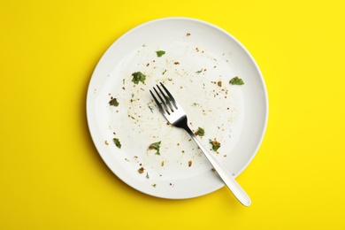 Photo of Dirty plate with food leftovers and fork on yellow background, top view