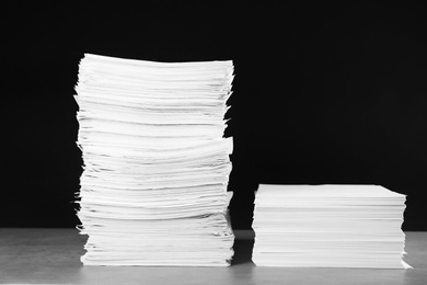 Photo of Stacks of blank paper on grey stone table against black background