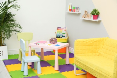 Stylish playroom interior with table, chairs and sofa