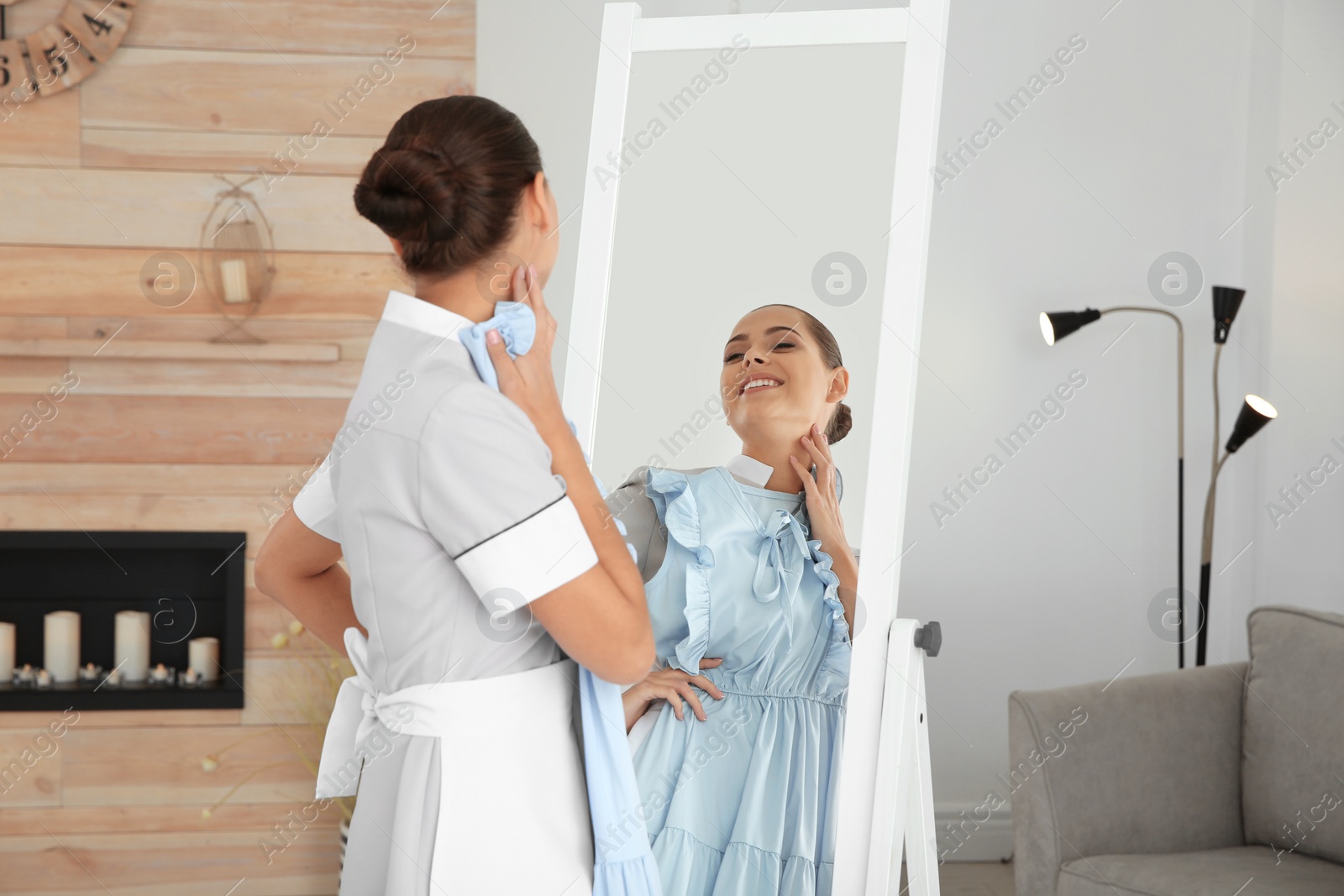 Photo of Young chambermaid trying on clothes near mirror in hotel room