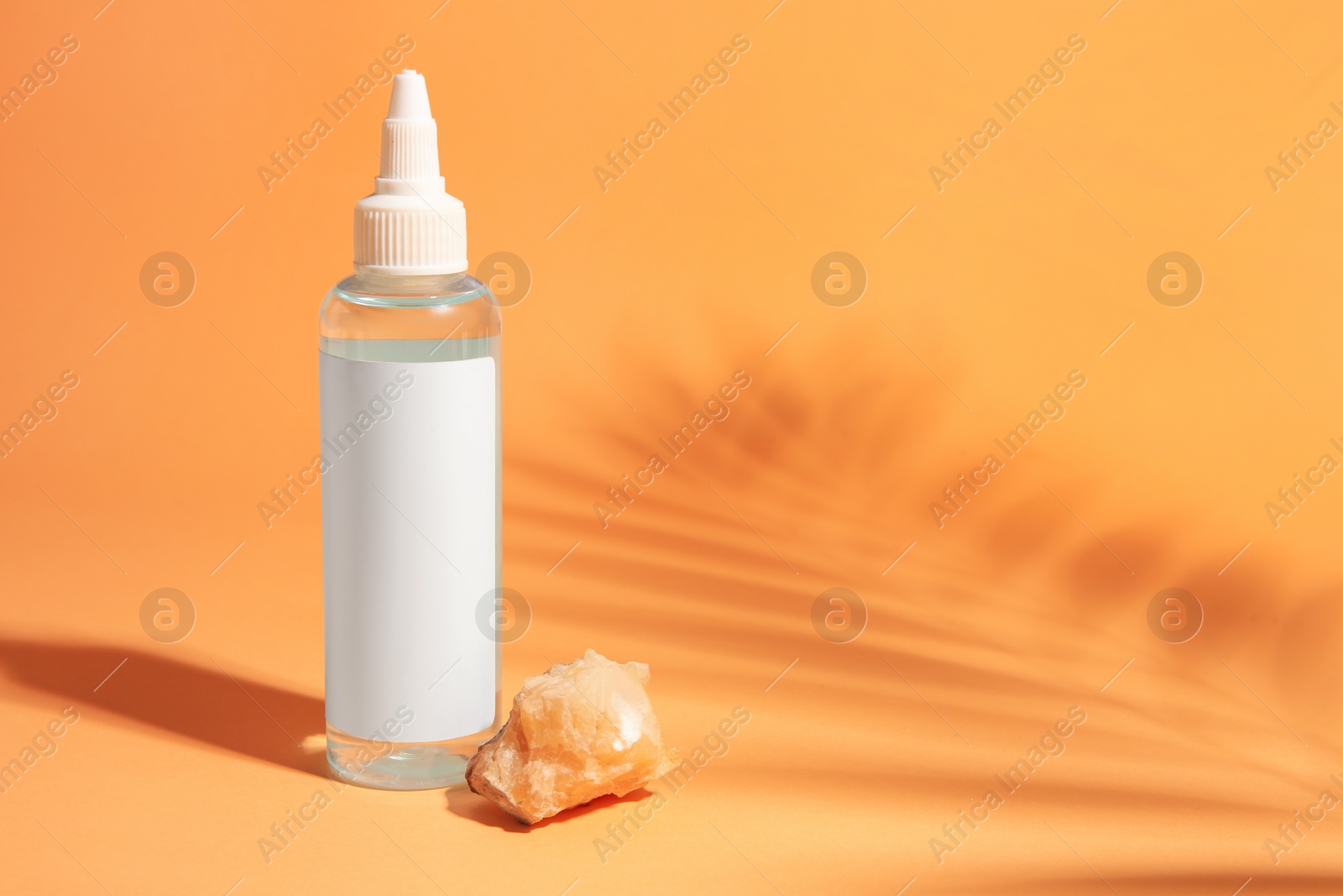 Photo of Cosmetic product and quartz gemstone on orange background, space for text
