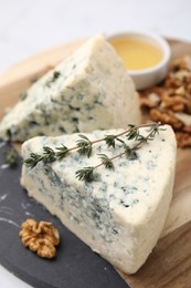 Tasty blue cheese with thyme, honey and walnuts on wooden board, closeup