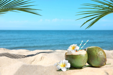 Image of Green coconuts with refreshing drink and flowers on sandy beach near sea, space for text