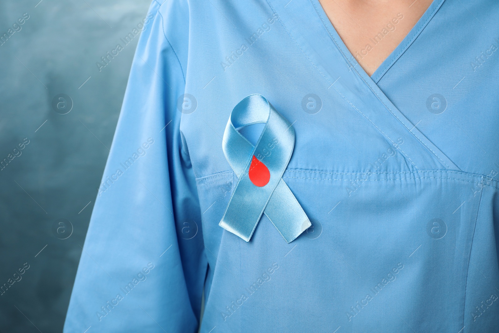 Photo of Doctor with light blue ribbon and paper blood drop on color background, closeup. World Diabetes Day