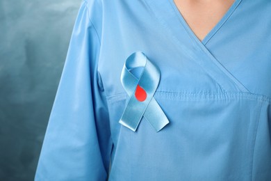 Photo of Doctor with light blue ribbon and paper blood drop on color background, closeup. World Diabetes Day