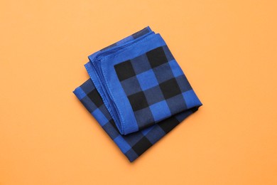 Photo of Folded blue checkered bandana on orange background, top view