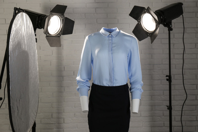 Photo of Stylish clothes on ghost mannequin and professional lighting equipment in modern studio. Fashion photography