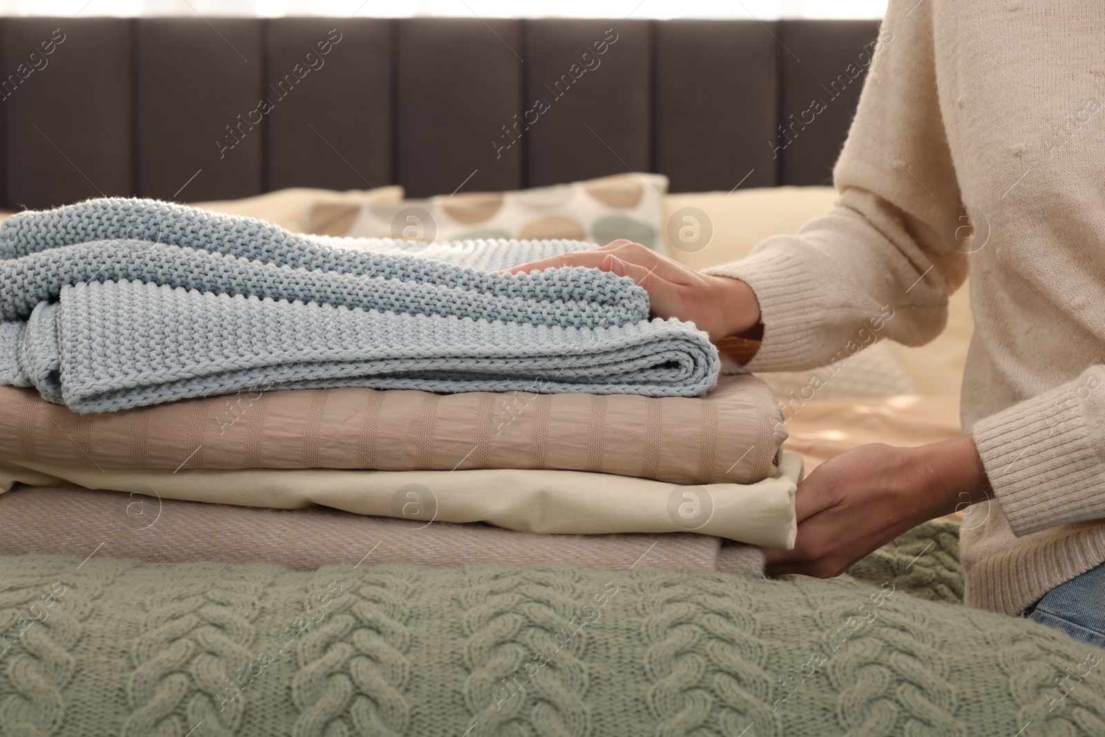 Photo of Woman with stack of different folded blankets on bed, closeup. Home textile