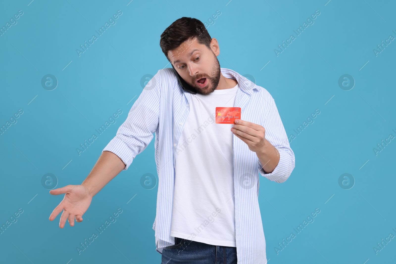 Photo of Emotional man with credit card talking on smartphone against light blue background. Be careful - fraud