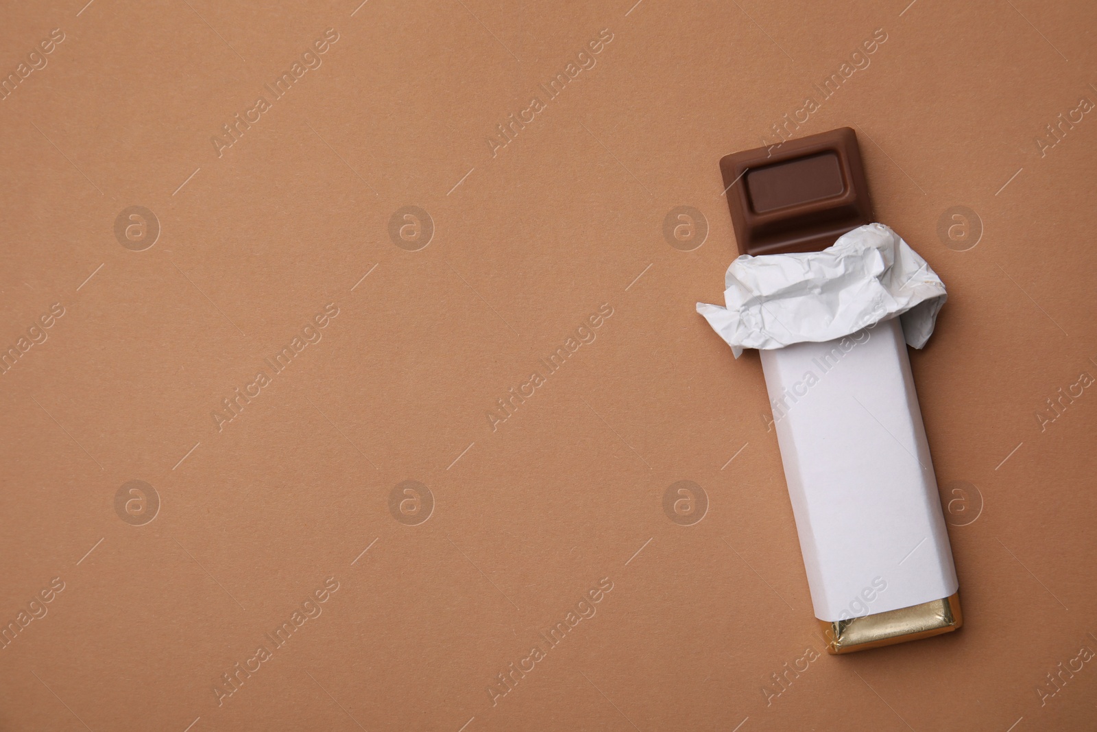Photo of Tasty chocolate bar in package on light brown background, top view. Space for text