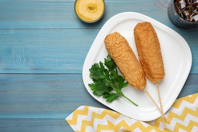 Photo of Delicious deep fried corn dogs with parsley and mustard on turquoise wooden table, flat lay. Space for text