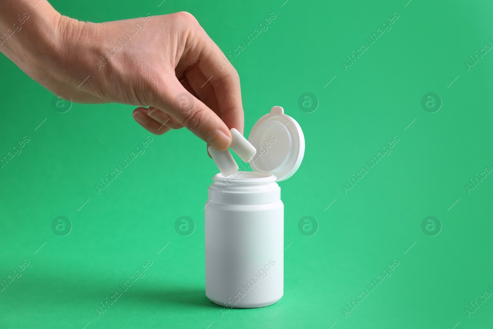 Photo of Woman taking chewing gums from jar on green background, closeup