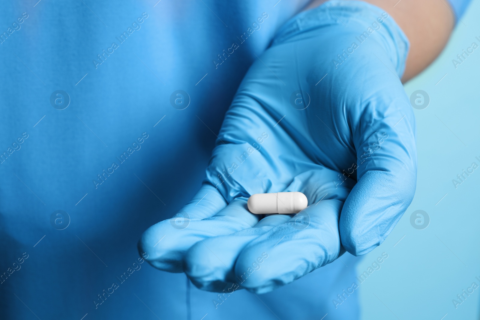 Photo of Doctor in medical glove holding pill on turquoise background, closeup