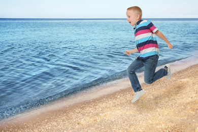 Image of Cute school boy jumping on beach near sea, space for text. Summer holidays