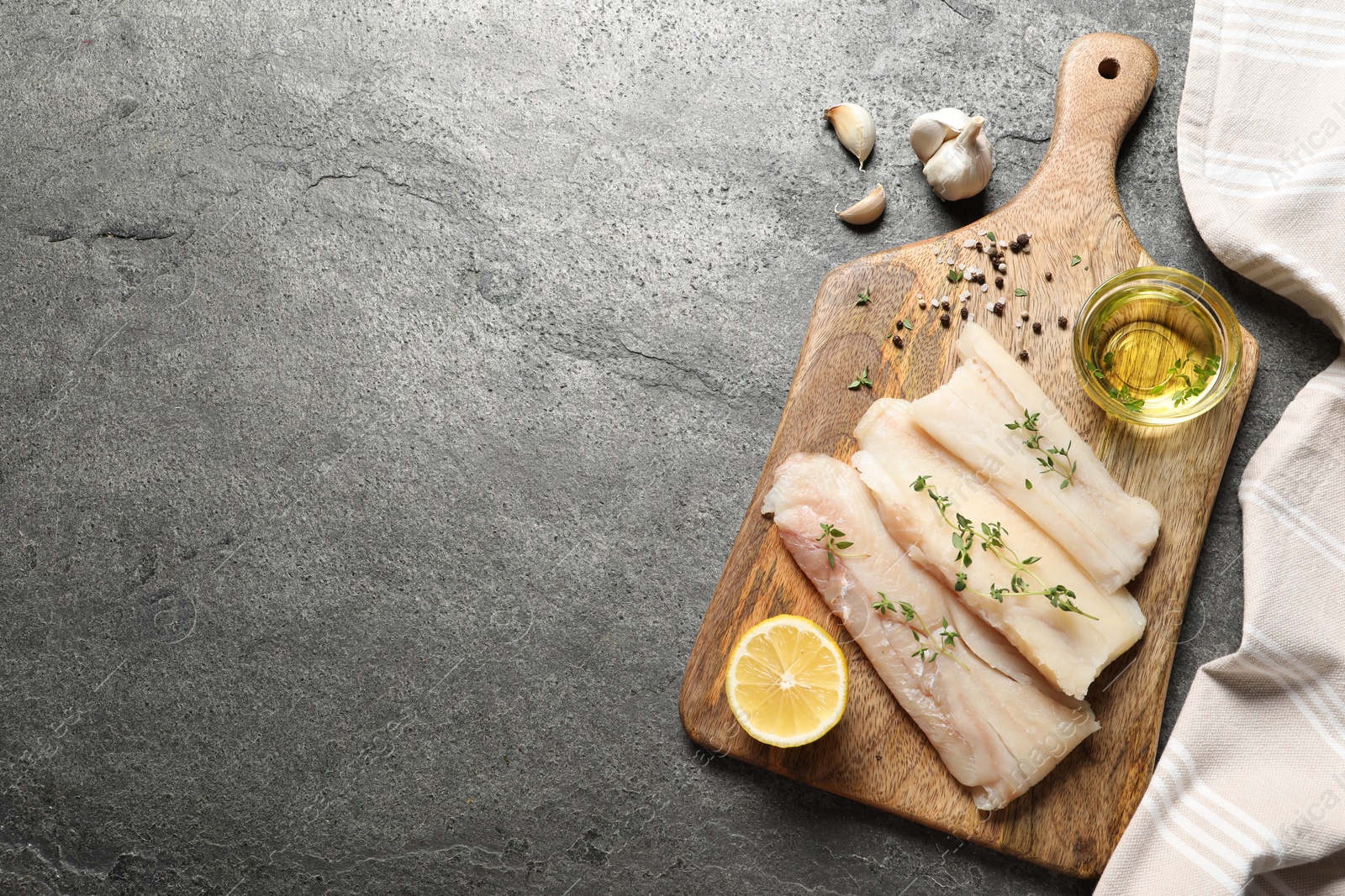 Photo of Raw cod fish, microgreens, oil, spices and lemon on grey textured table, top view. Space for text