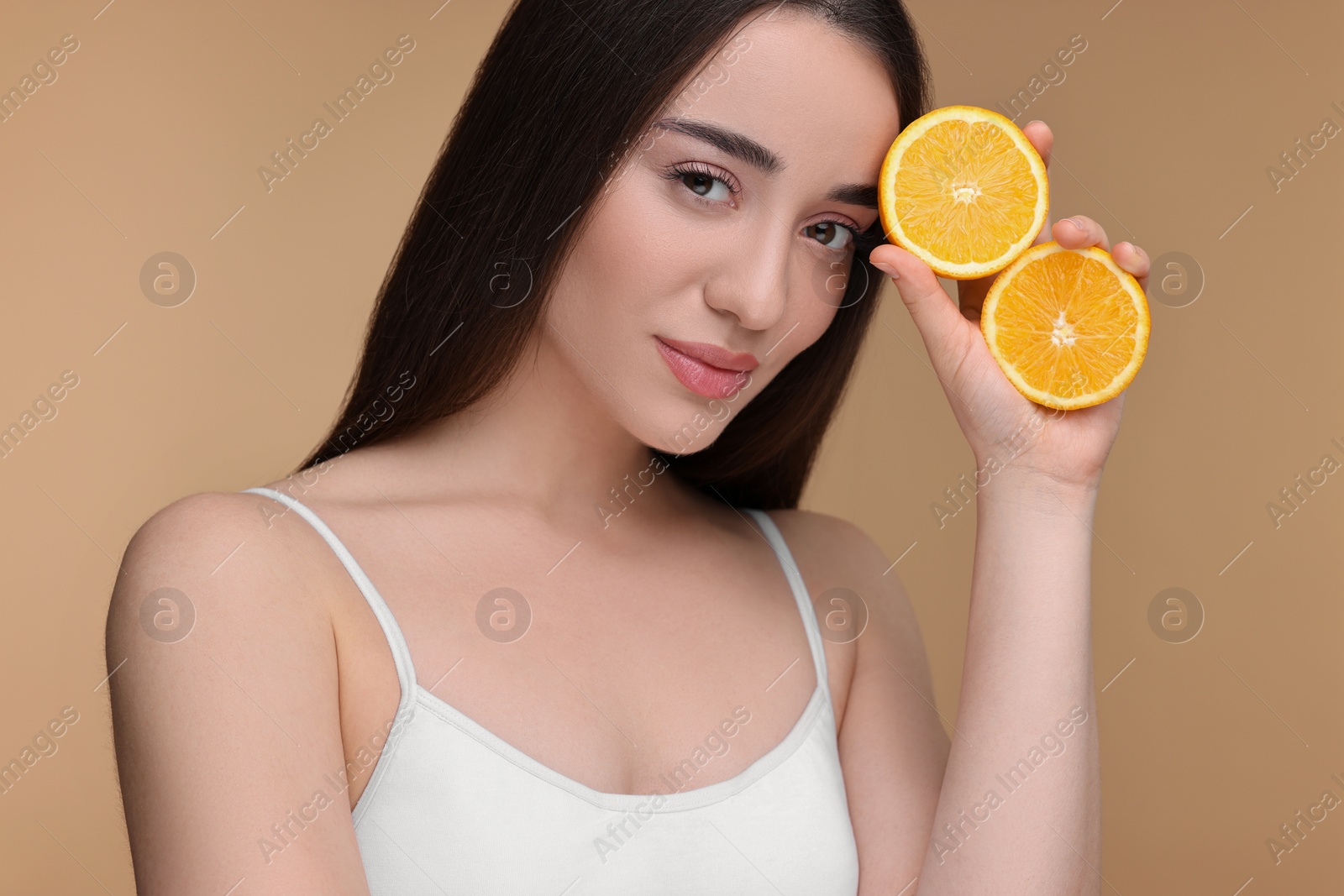 Photo of Beautiful young woman with pieces of orange on beige background