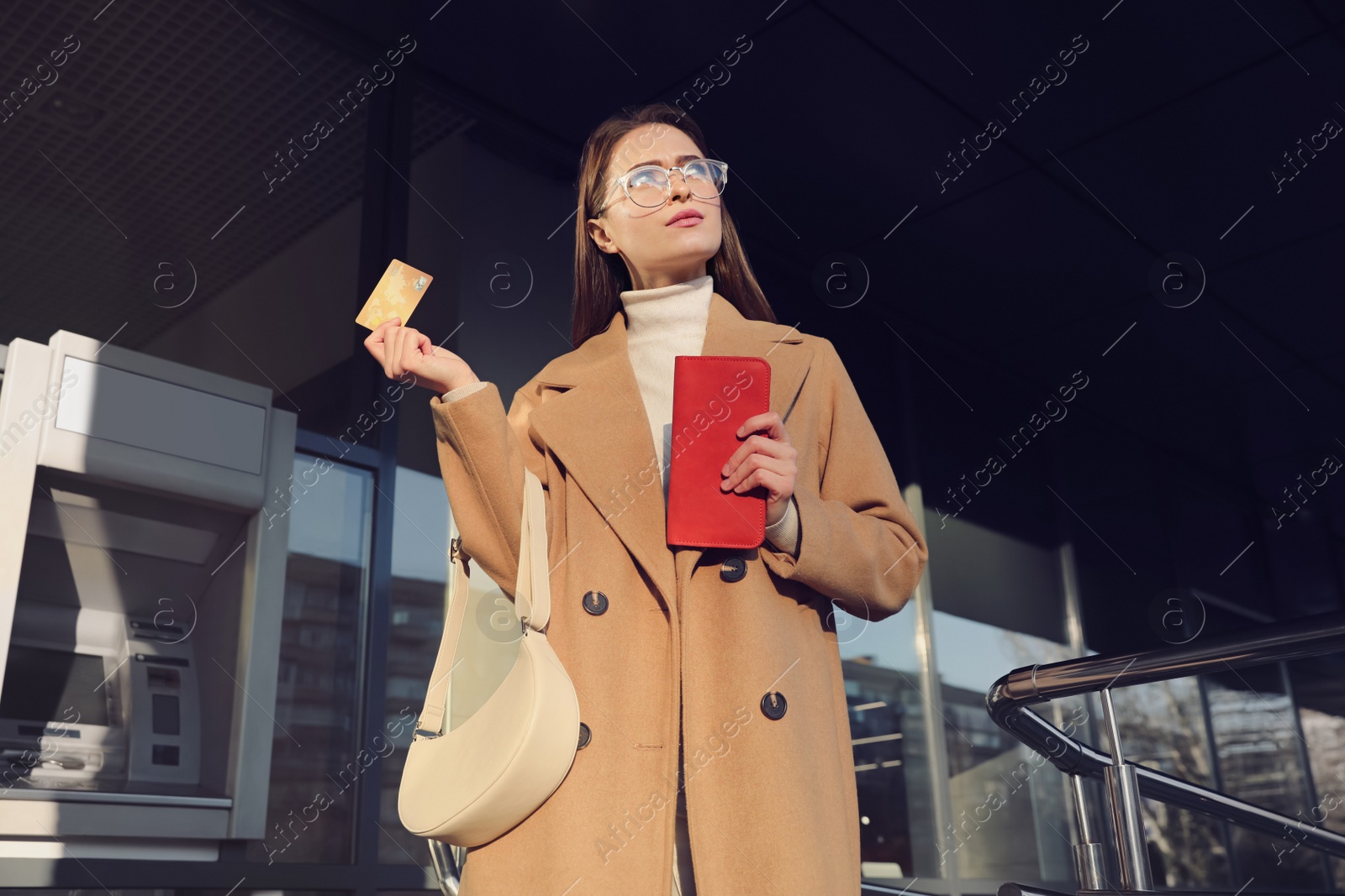 Photo of Young woman with credit card near cash machine outdoors