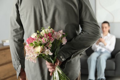 Photo of Man hiding bouquet of flowers for his beloved woman indoors, closeup