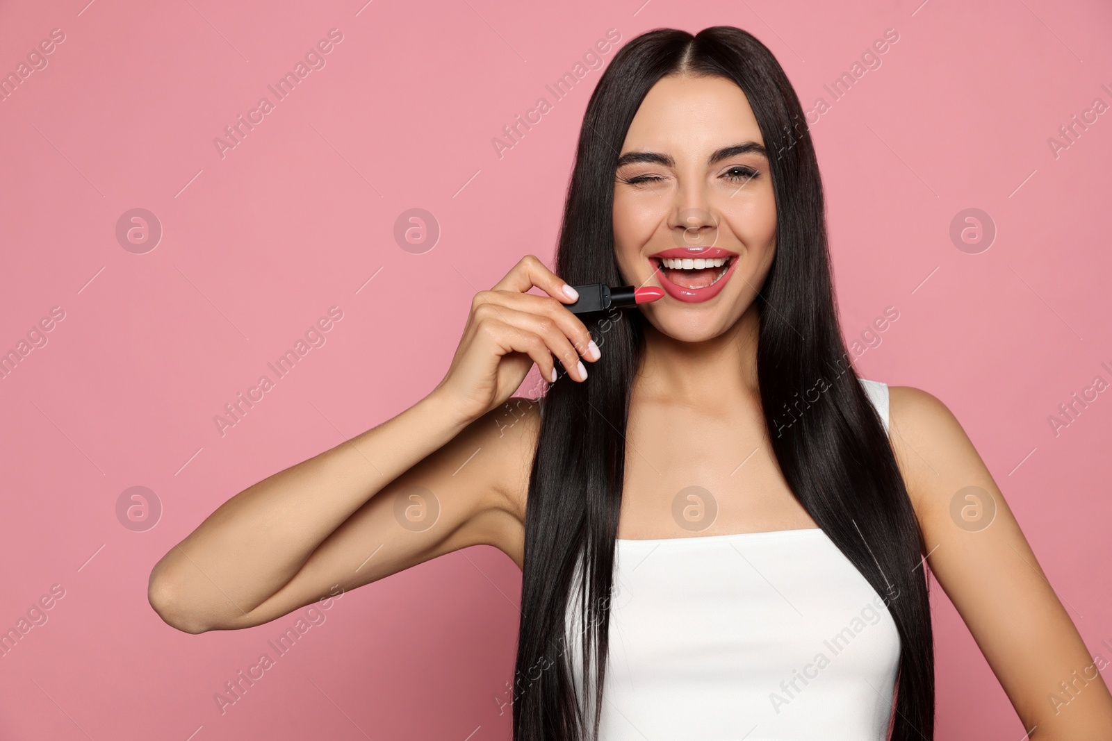 Photo of Emotional young woman with beautiful makeup holding glossy lipstick on pink background