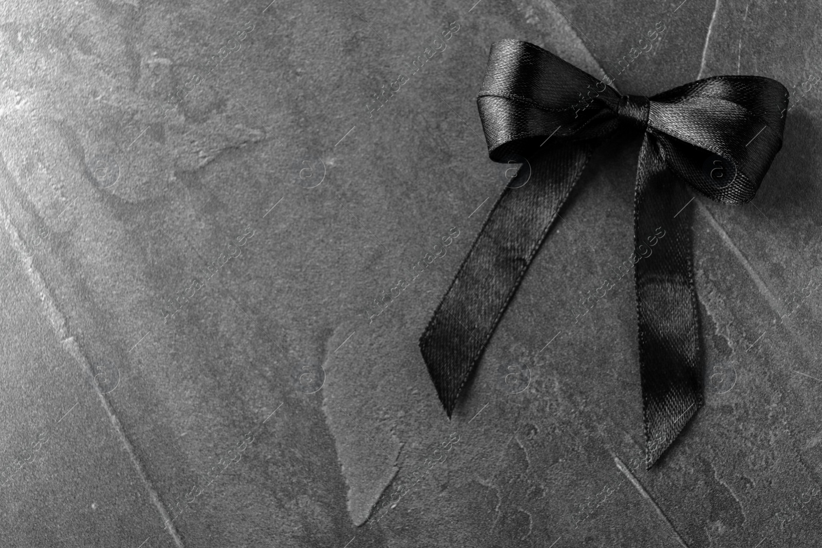 Photo of Black ribbon bow on dark grey stone surface, top view with space for text. Funeral symbol