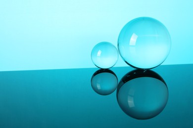 Photo of Transparent glass balls on mirror surface against turquoise background. Space for text