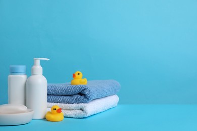 Photo of Baby cosmetic products, bath ducks and towels on light blue background. Space for text