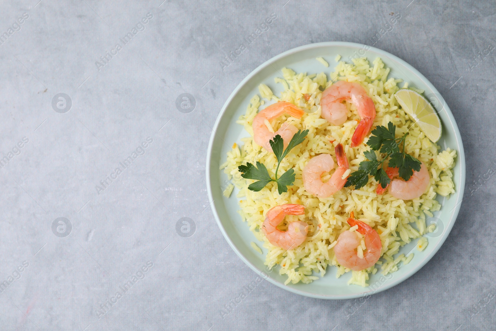 Photo of Delicious risotto with shrimps, lime and parsley on light grey table, top view. Space for text