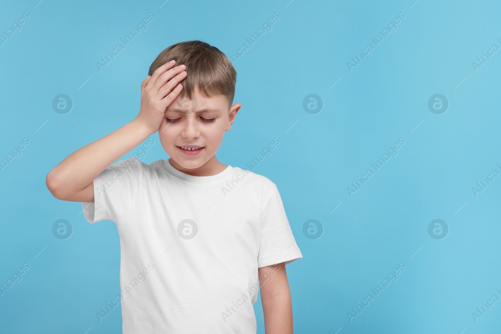 Photo of Little boy suffering from headache on light blue background, space for text