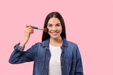 Photo of Beautiful woman applying makeup with brush on pink background