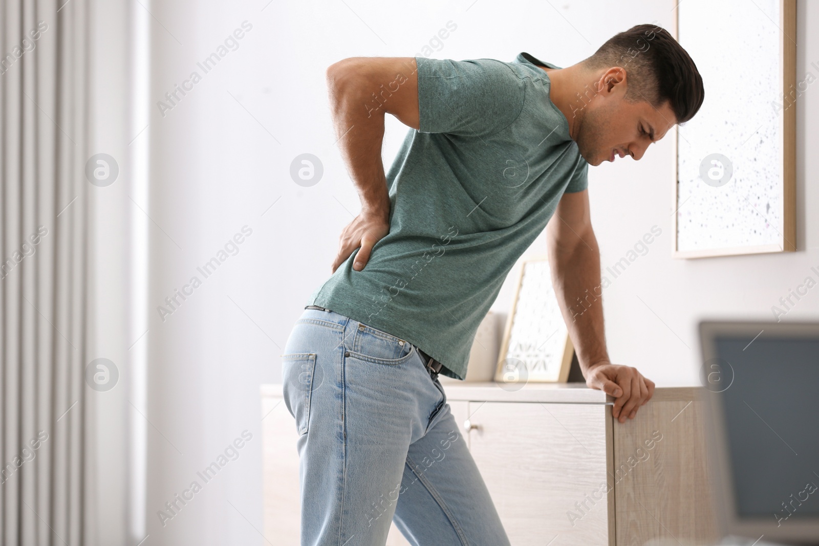 Photo of Man suffering from back pain at home. Bad posture problem