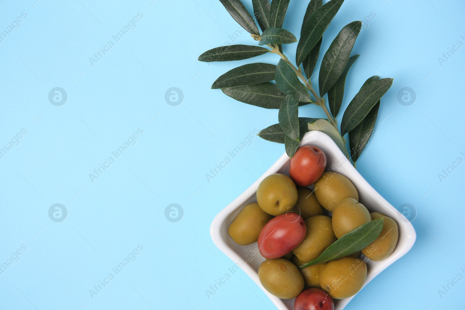 Photo of Different fresh olives and green leaves on light blue background, flat lay. Space for text