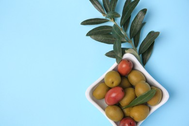 Different fresh olives and green leaves on light blue background, flat lay. Space for text