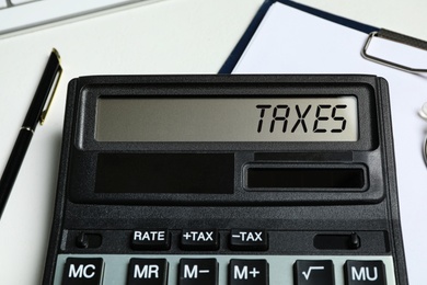 Calculator with word Taxes, documents and pen on table, closeup