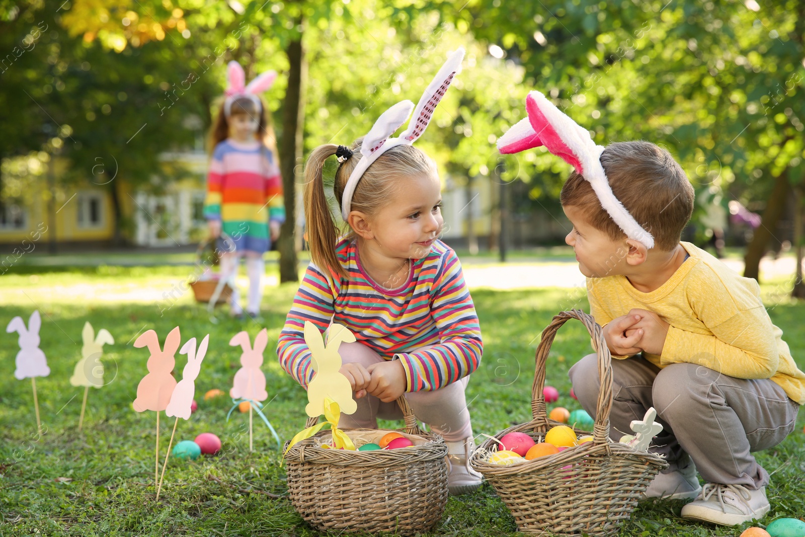 Photo of Cute little children hunting eggs in park. Easter tradition