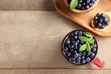 Photo of Tasty fresh bilberries with green leaves on wooden table, flat lay. Space for text