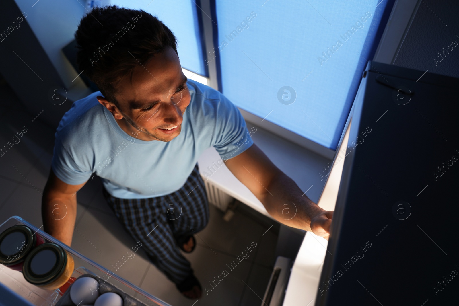 Photo of Man taking products out of refrigerator in kitchen at night, high angle view