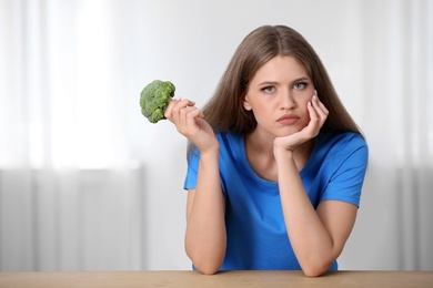 Photo of Portrait of unhappy woman with broccoli at table indoors