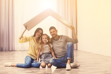 Image of Happy family sitting under cardboard roof at home. Insurance concept