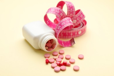 Photo of Jar of weight loss pills and measuring tape on beige background