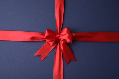 Photo of Red satin ribbon with bow on blue background, top view