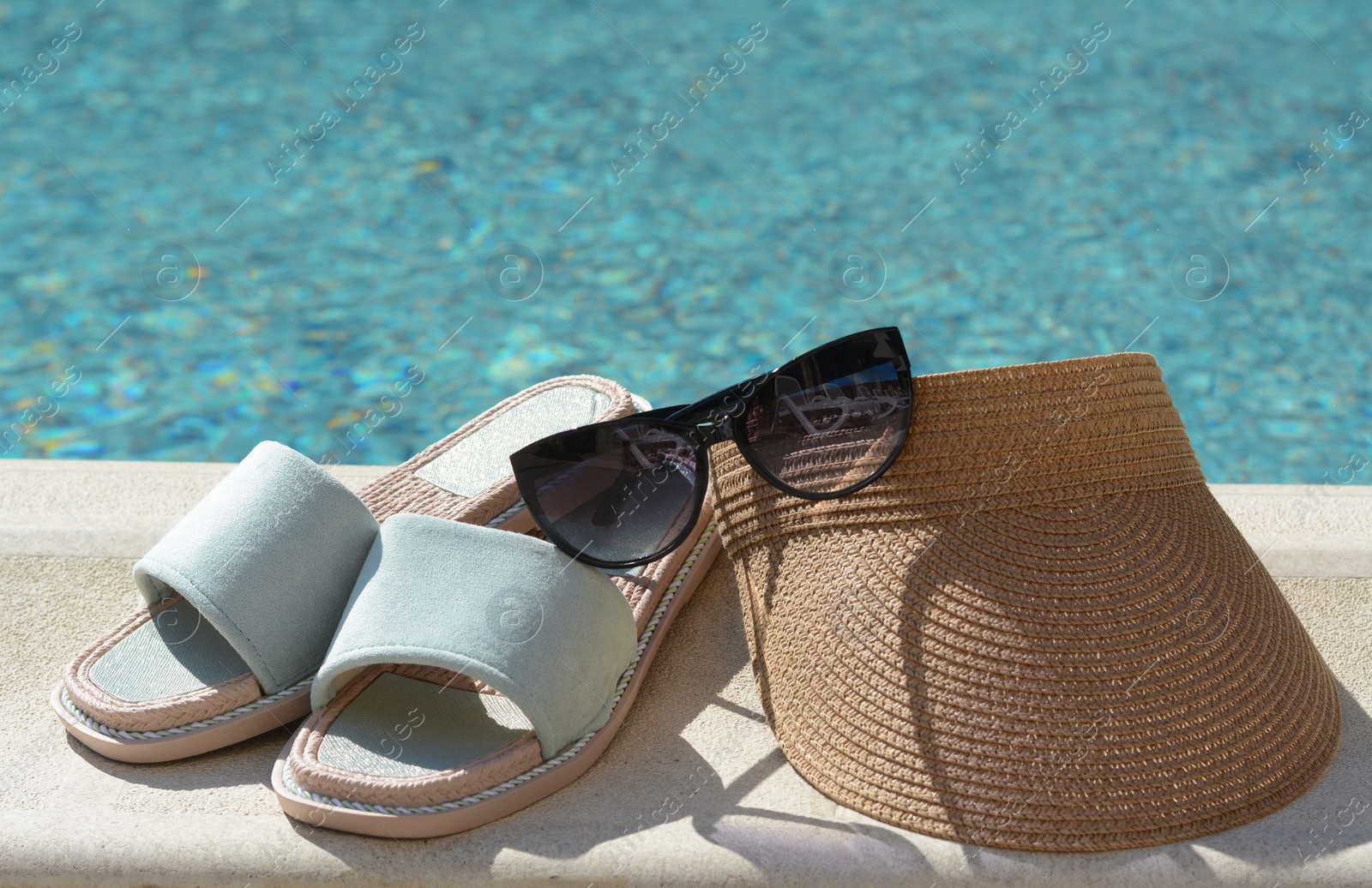 Photo of Stylish sunglasses, visor cap and slippers at poolside on sunny day. Beach accessories