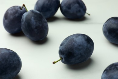 Many tasty ripe plums on white table, closeup