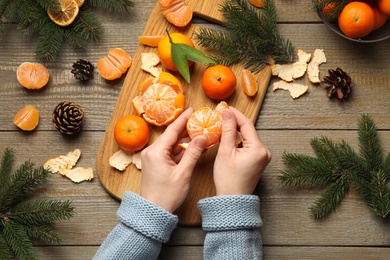 Photo of Woman peeling fresh tangerine at wooden table, top view. Christmas atmosphere